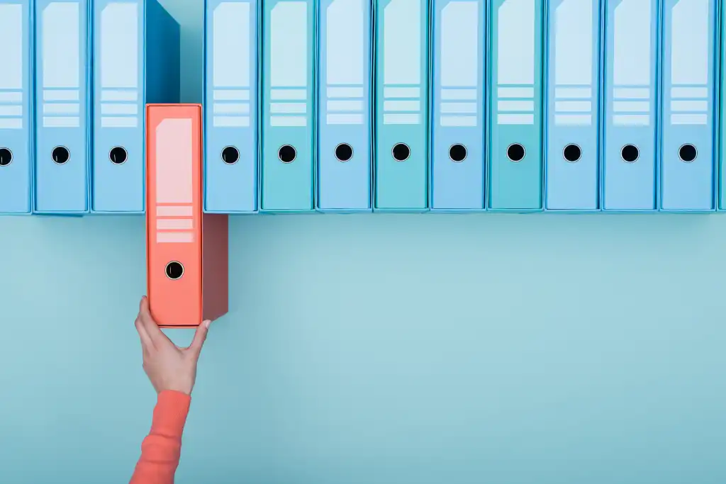 Choosing a database. Red-sleeved arm pulls red binder from a row of blue binders against a blue green background.