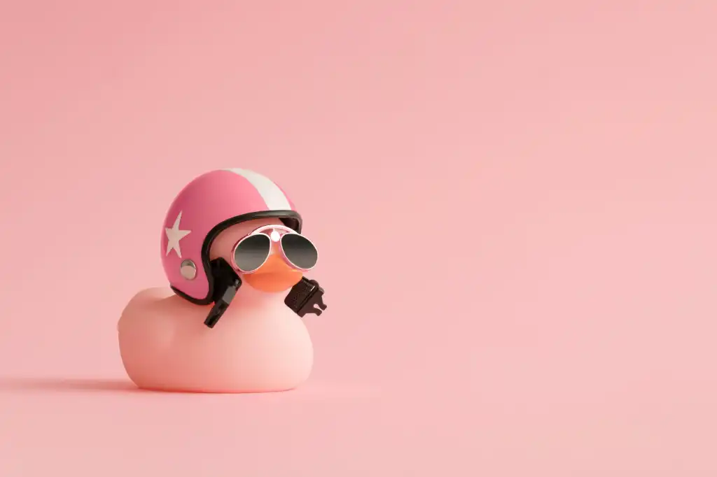 Creative composition made of pink cute little rubber duckling with a helmet and sunglasses on pink background. Summer minimal duck concept.