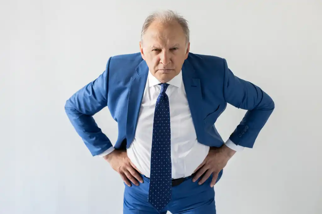 Portrait of frowning mature businessman looking at camera. Senior manager wearing formalwear standing with hands on hips against white background. Angry boss concept